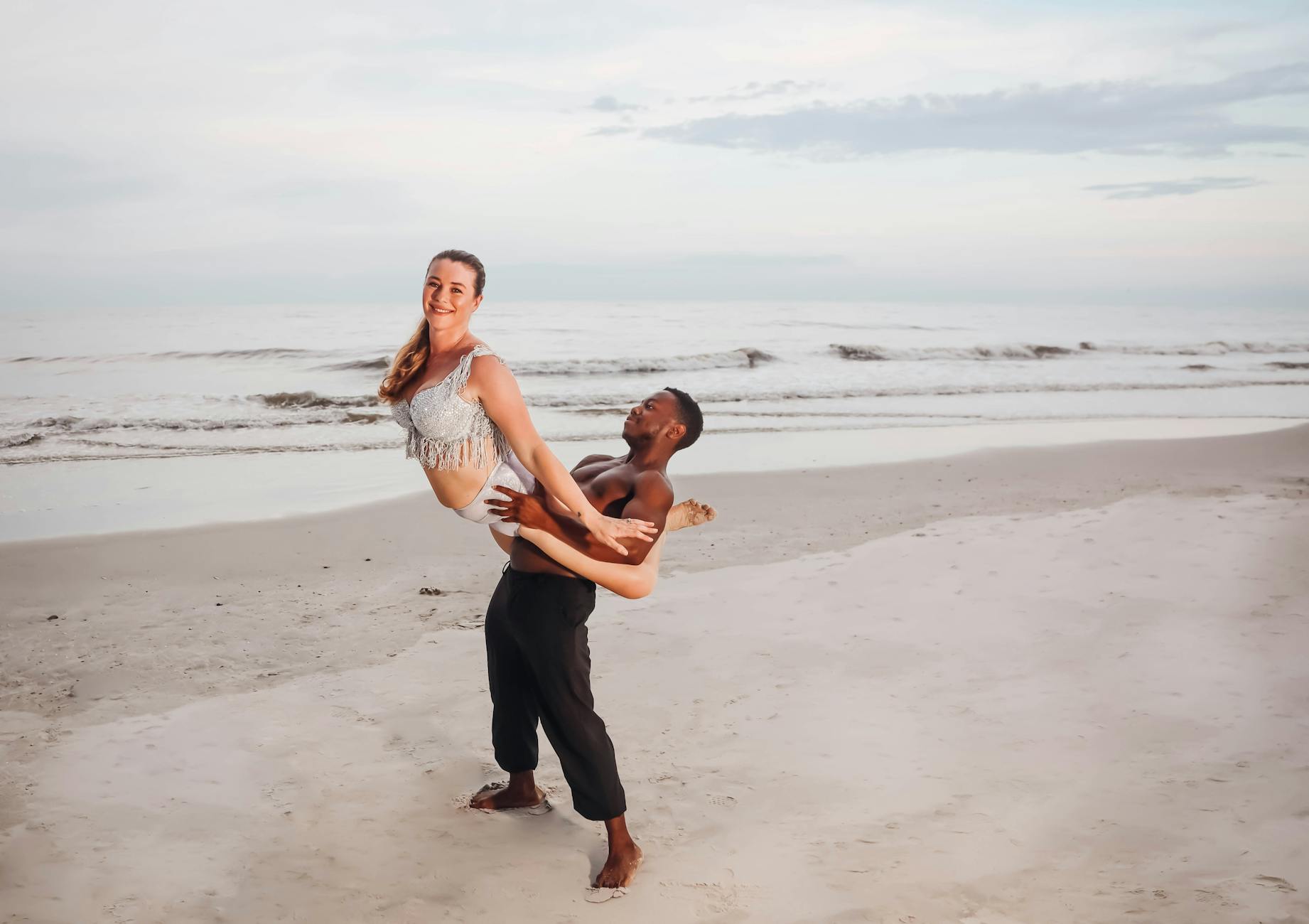 A joyful couple dances playfully on a sandy Florida beach at sunset, celebrating life.