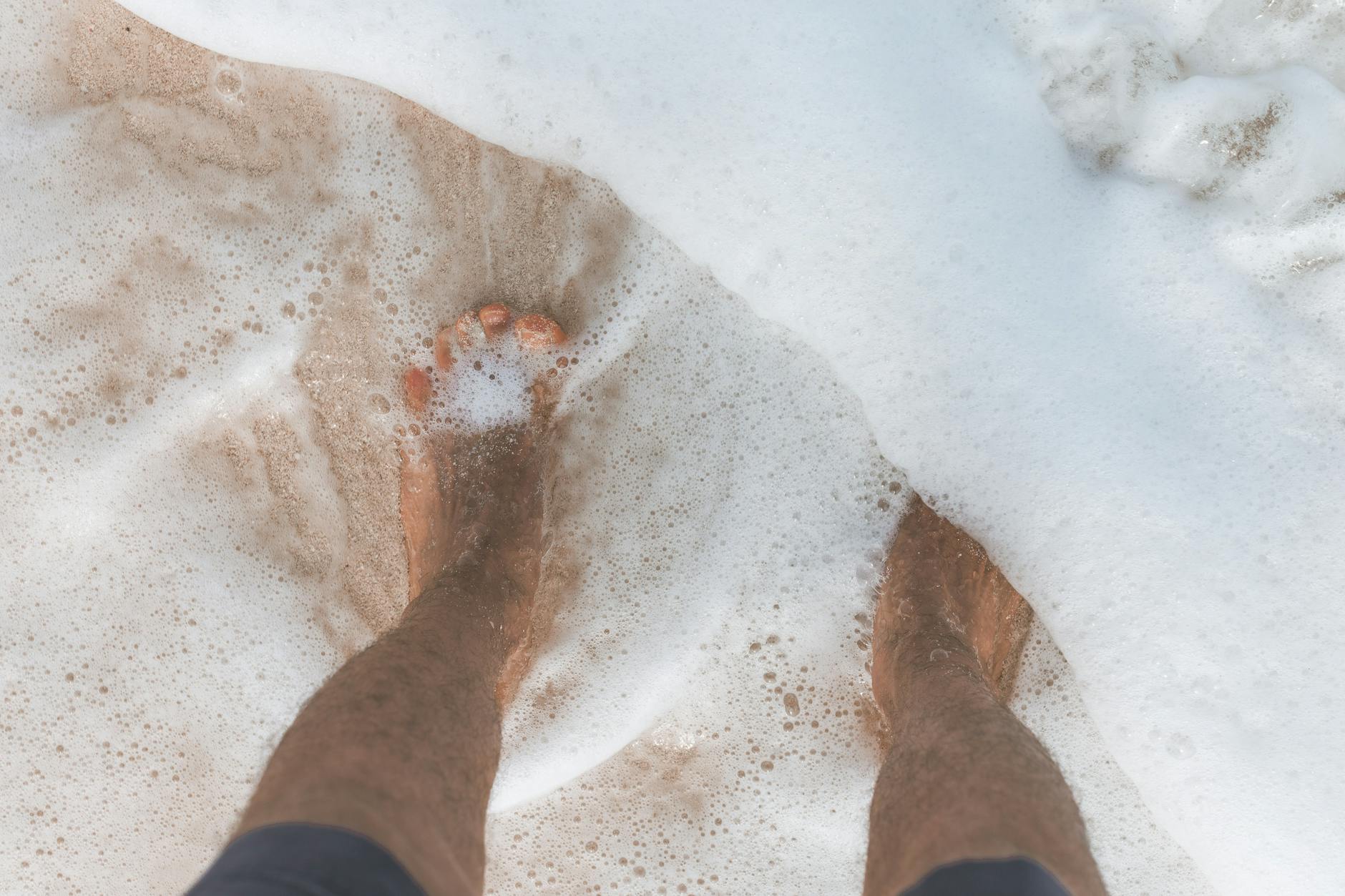 Capture the essence of relaxation with feet immersed in foamy waves on a sandy beach.