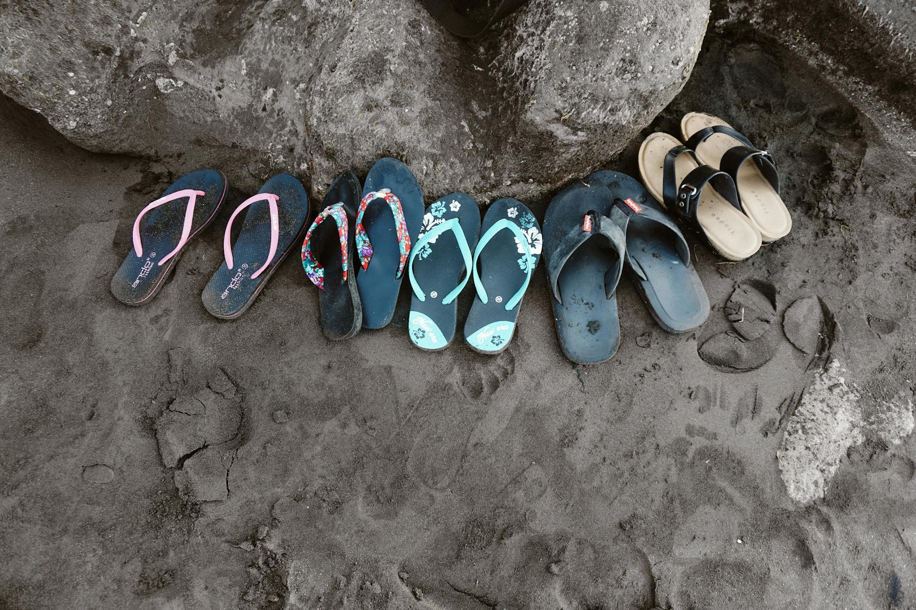 A collection of vibrant flip flops left on the sand in Bali, Indonesia, depicting a casual beach vibe.
