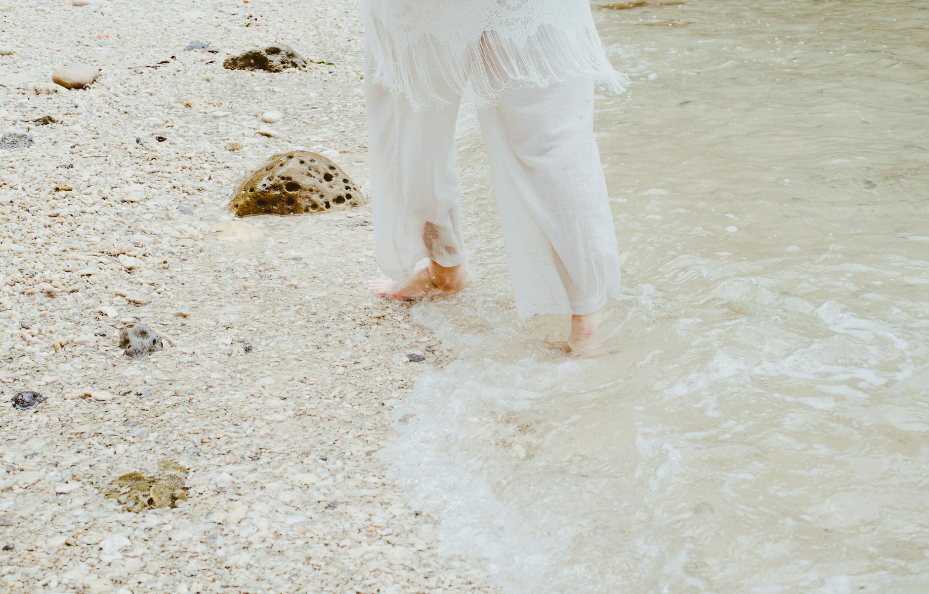 A serene moment of walking barefoot on a rocky beach with gentle waves in summer.