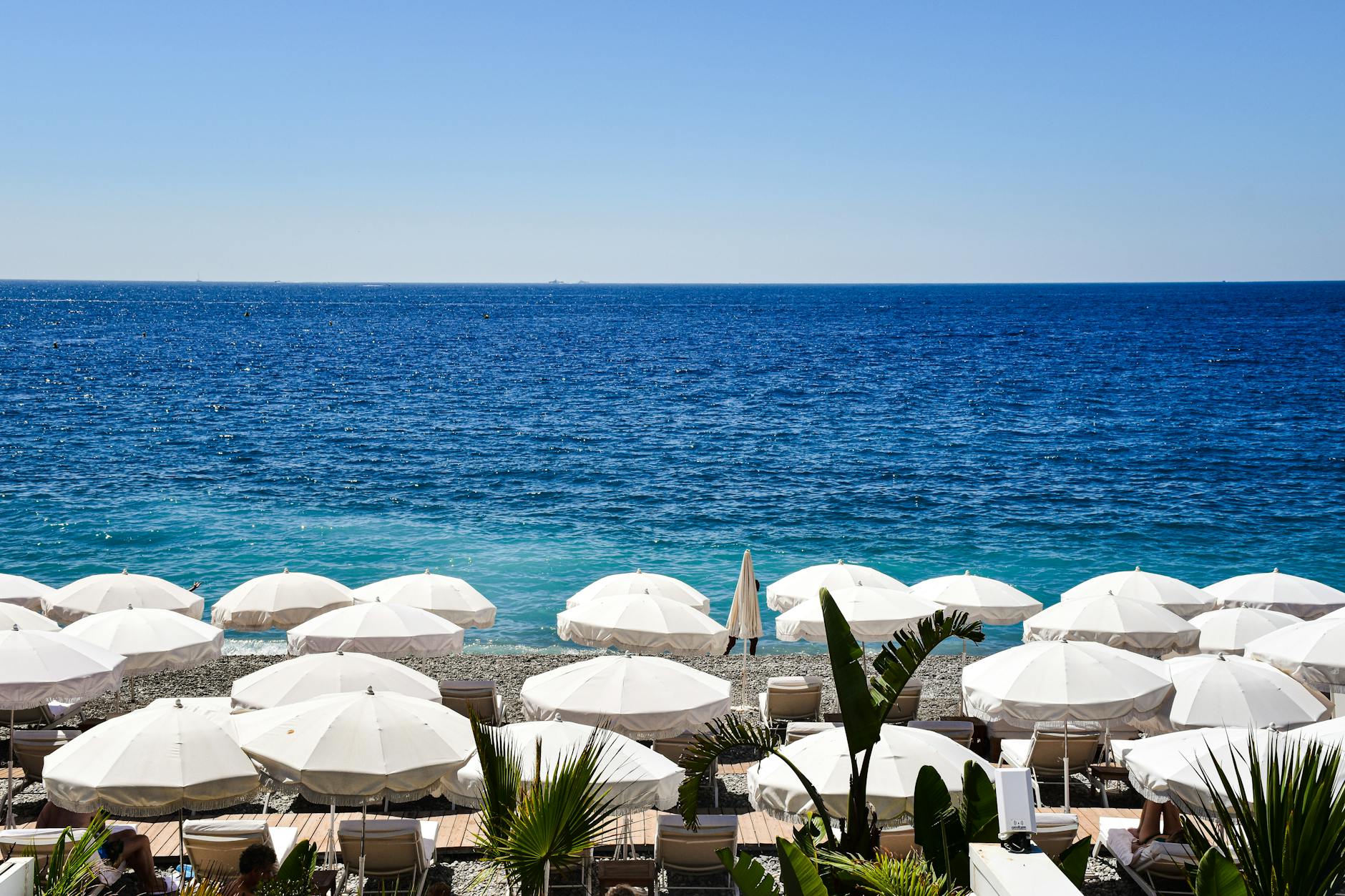Sunny day at a picturesque beach in Provence-Alpes-Côte d'Azur, France, with white umbrellas and blue sea.