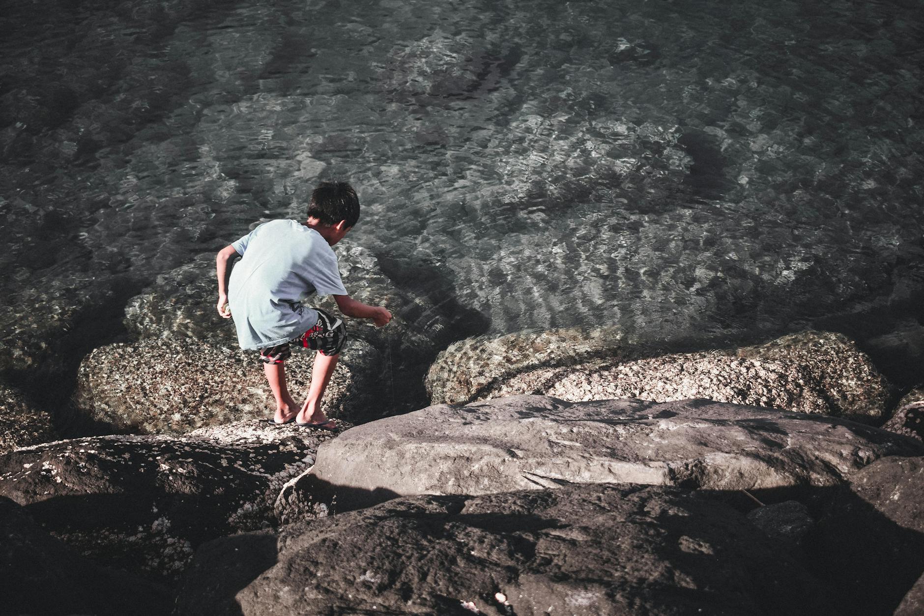 A child exploring rocks by the clear sea in daylight, capturing adventure and exploration.