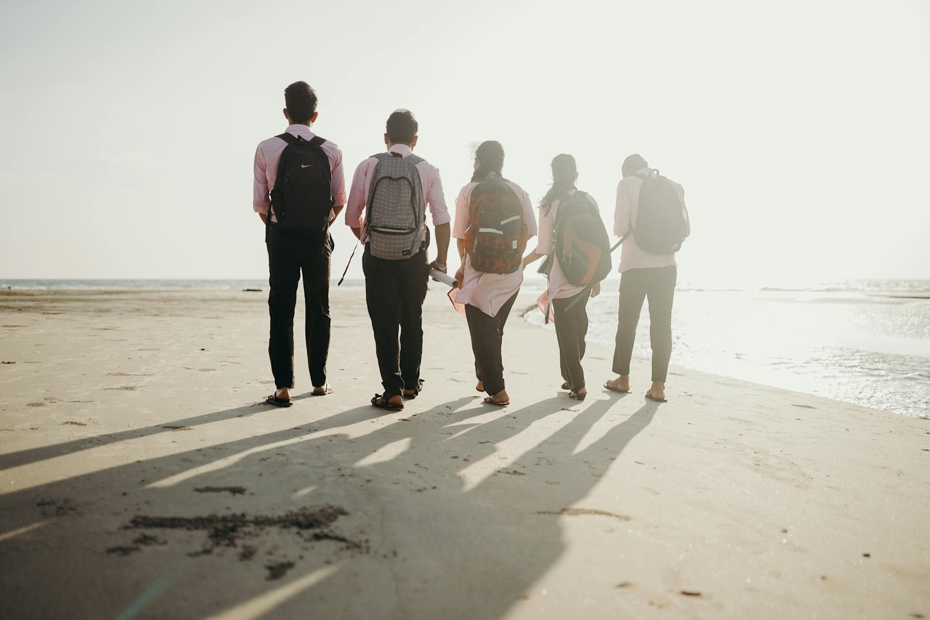 A group of friends with backpacks enjoys a sunny day walking along the beach shoreline.