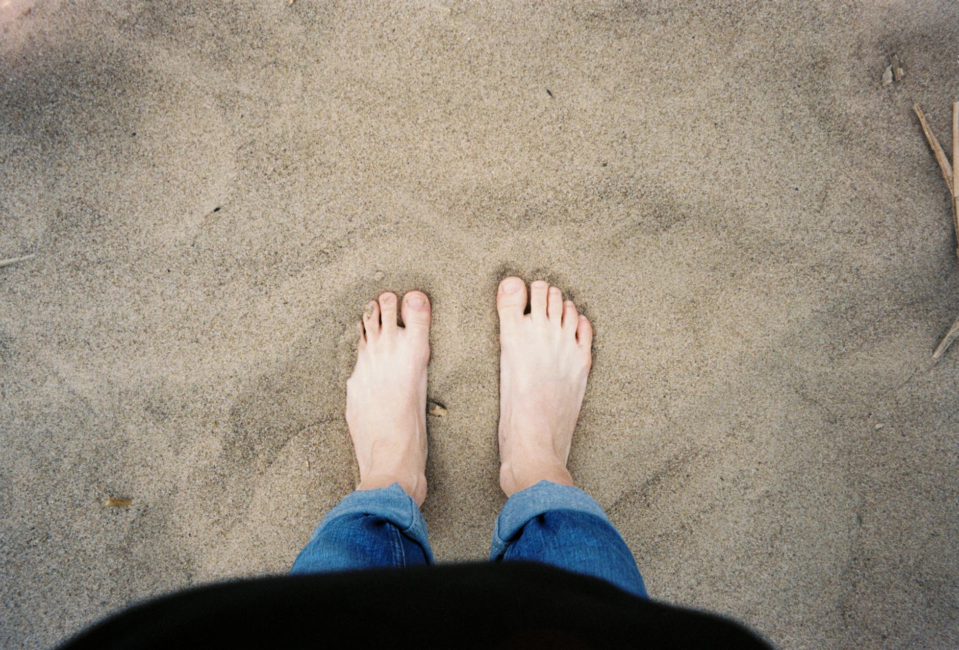 Top view of bare feet standing on sand, capturing a relaxed beach vibe.