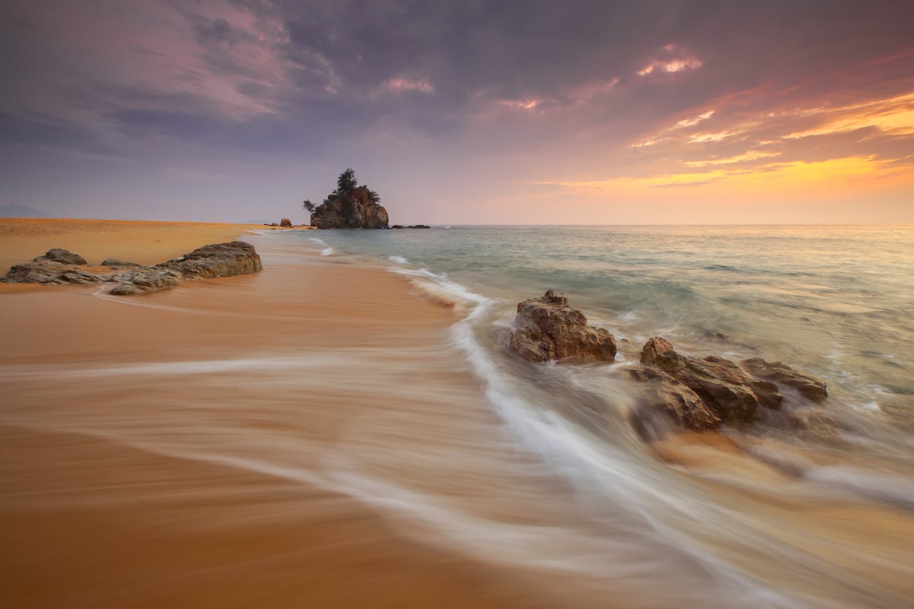 who-we-are Tranquil beach scene at sunrise with soft waves and rock formations.