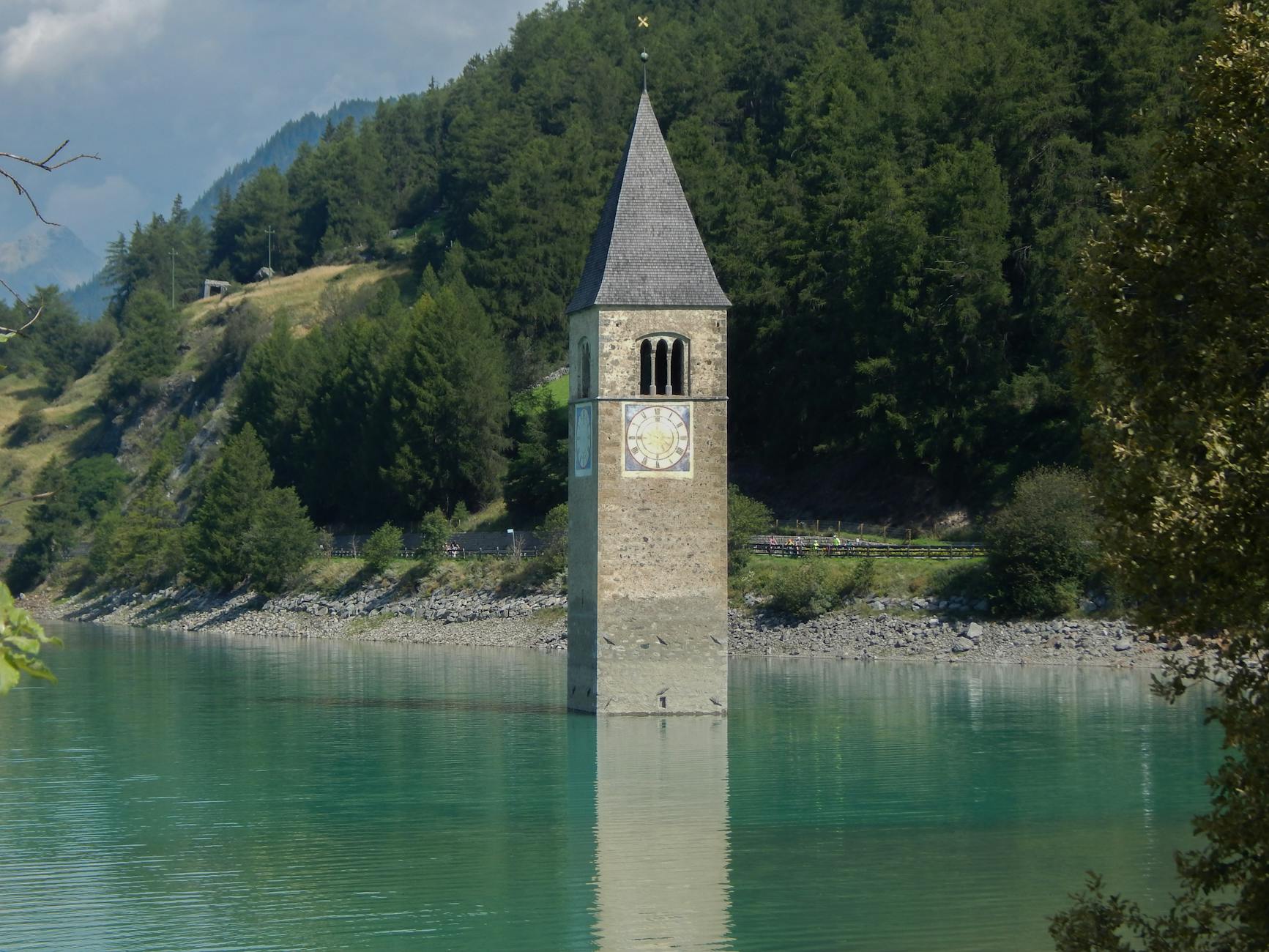 Aged building facade surrounded by calm water near hills covered with green forest in sunny summer day