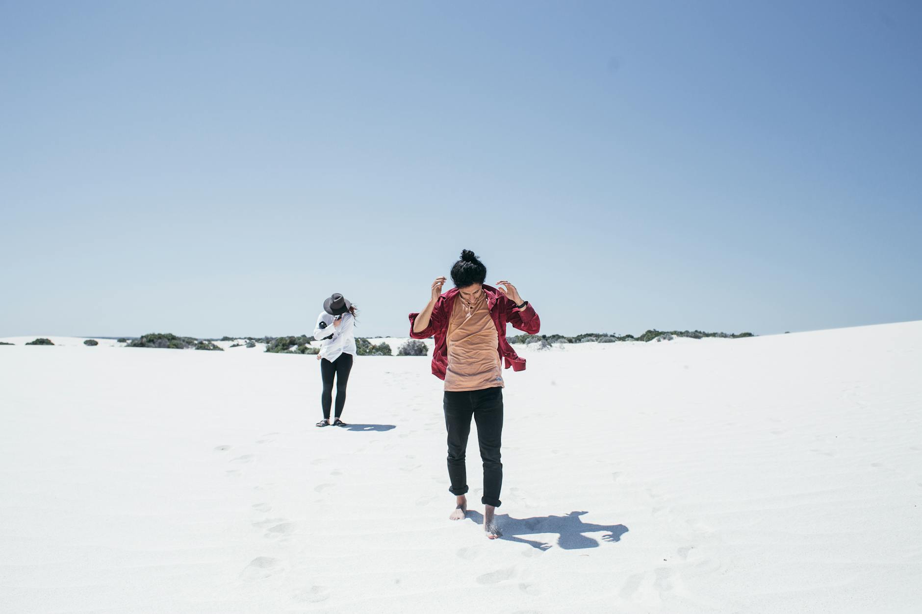 Two people walk across a vast white sandy desert on a sunny day, capturing the essence of exploration and adventure.