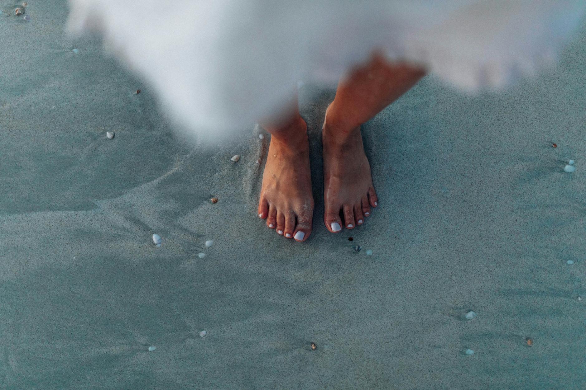 Close-up of woman's feet on sand near the ocean, creating a serene summer vibe.