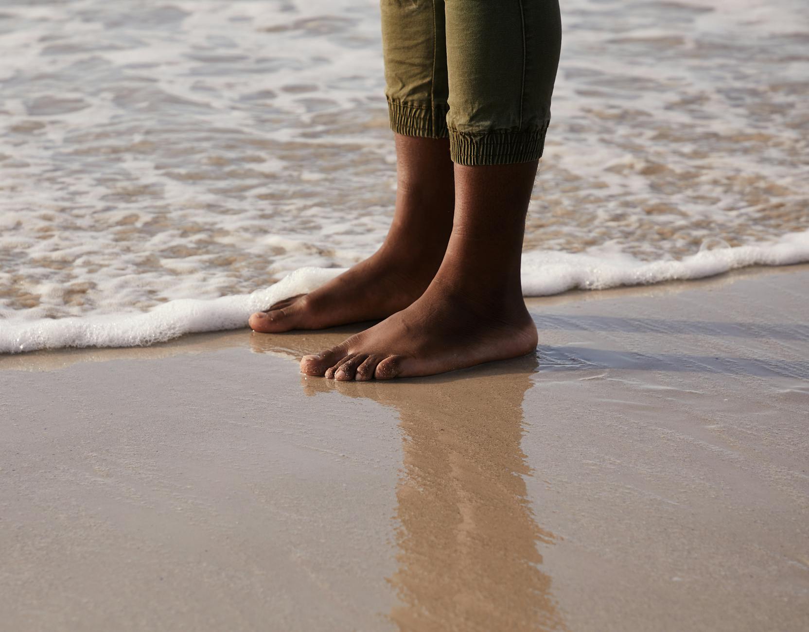 Crop anonymous ethnic tourist reflecting on sandy beach near foamy sea in stormy weather